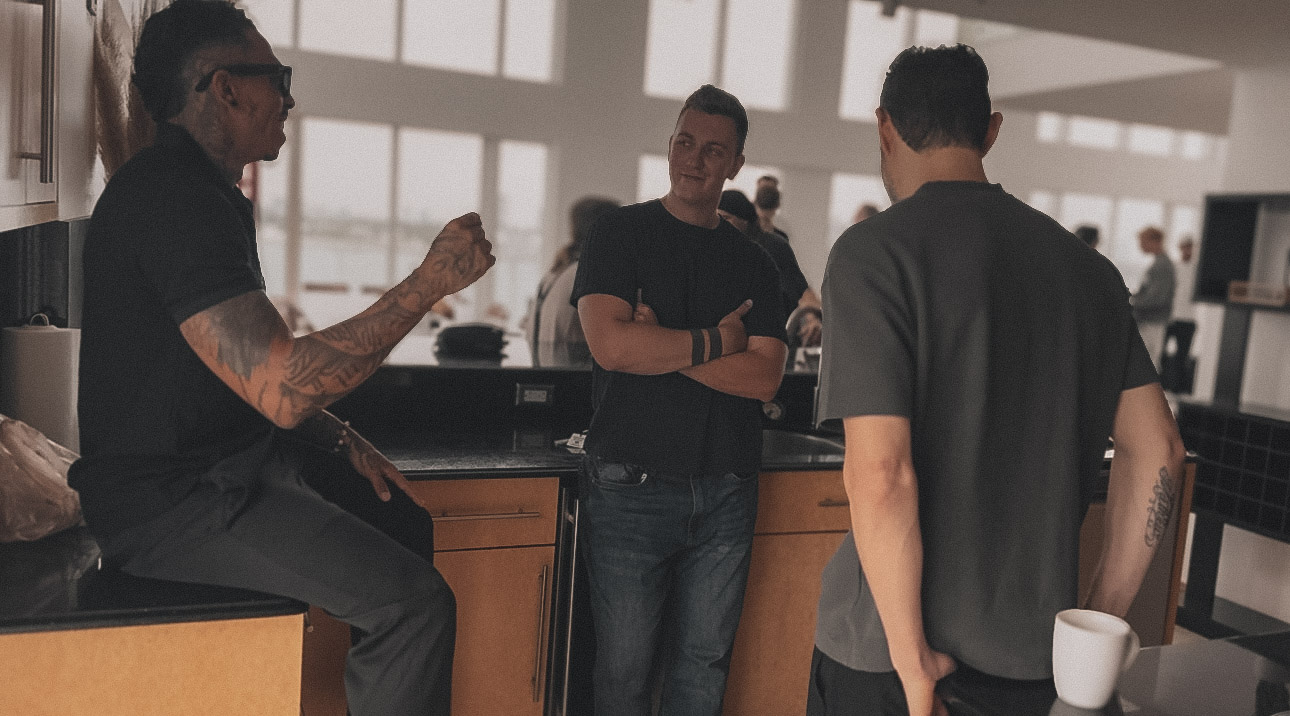 Three men talking in a kitchen during a morning gathering