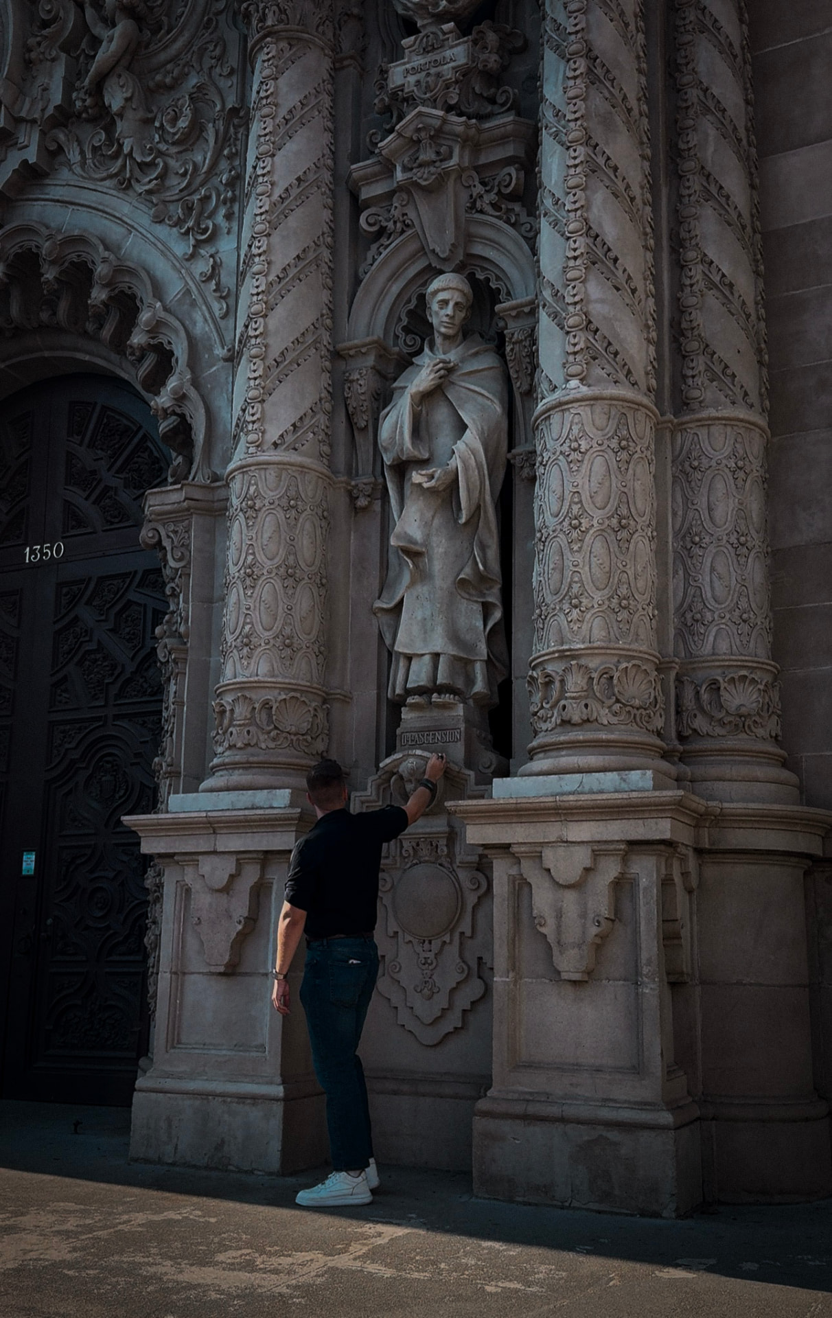 A man reaching up to touch a carved stone statue on an ornate cathedral facade